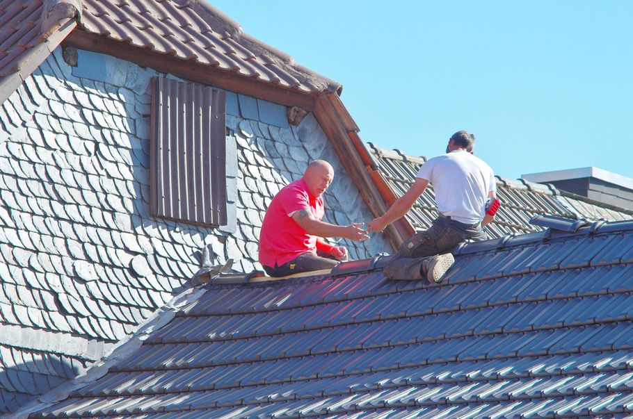 Two workers on a roof installing shingles on a sunny day