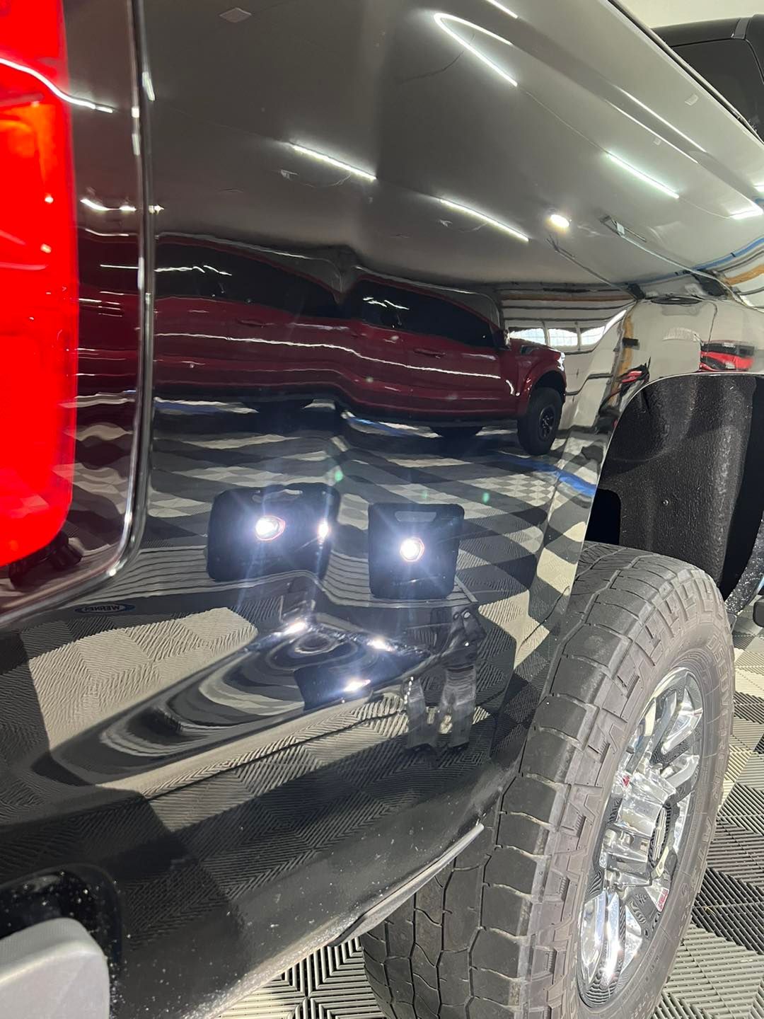 A red truck is parked in a garage next to a black truck.