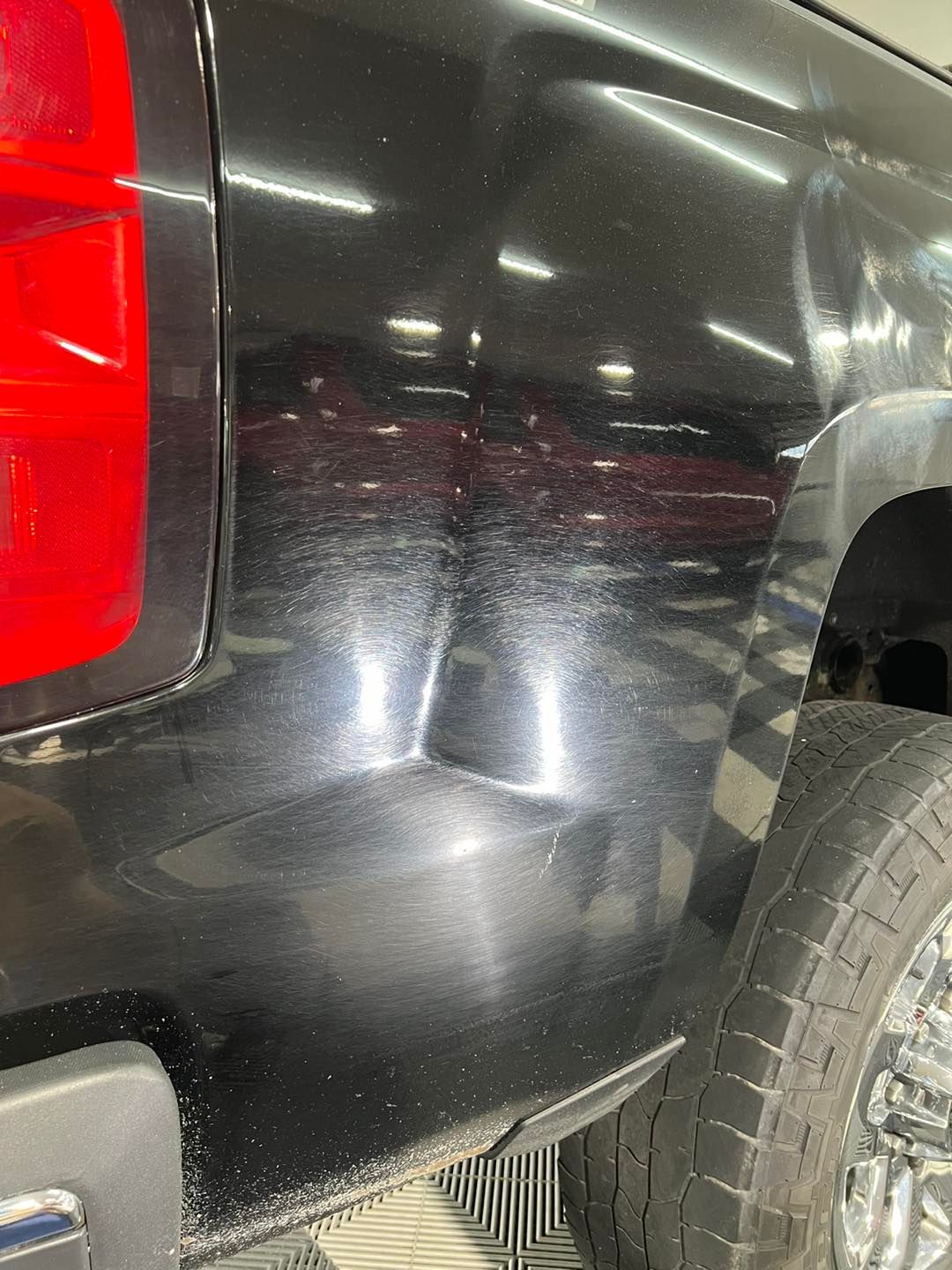 A black truck with a red tail light is parked in a garage.