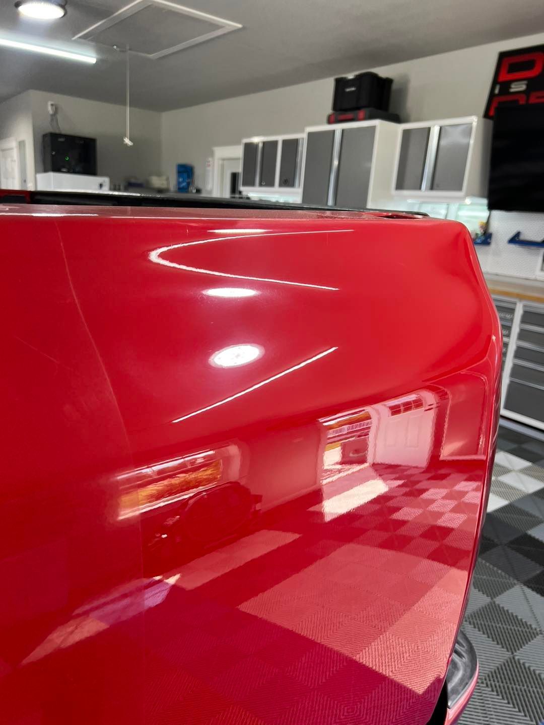 A red car is parked in a garage with a checkered floor.