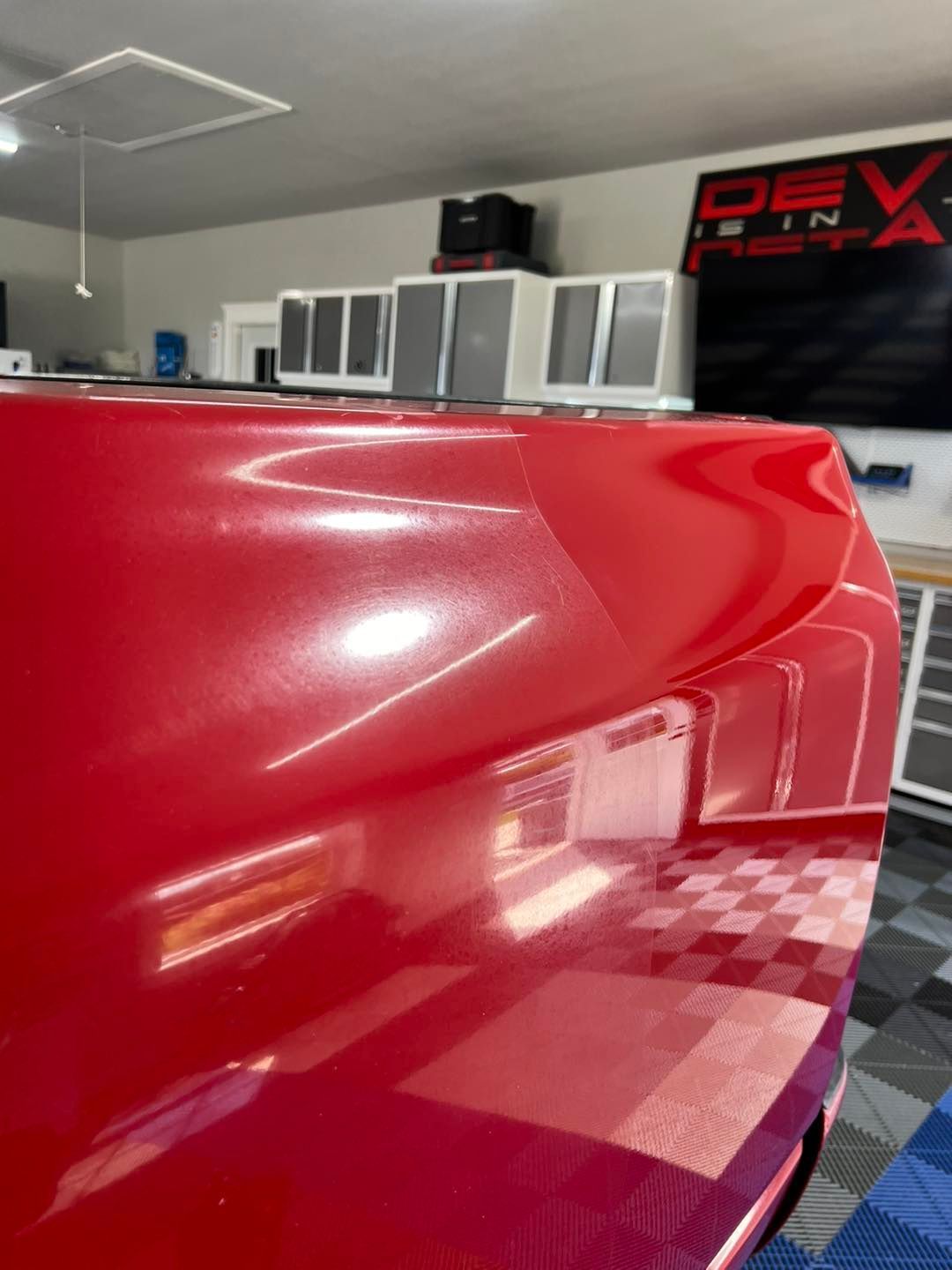 A close up of a red car 's fender and hood in a garage.