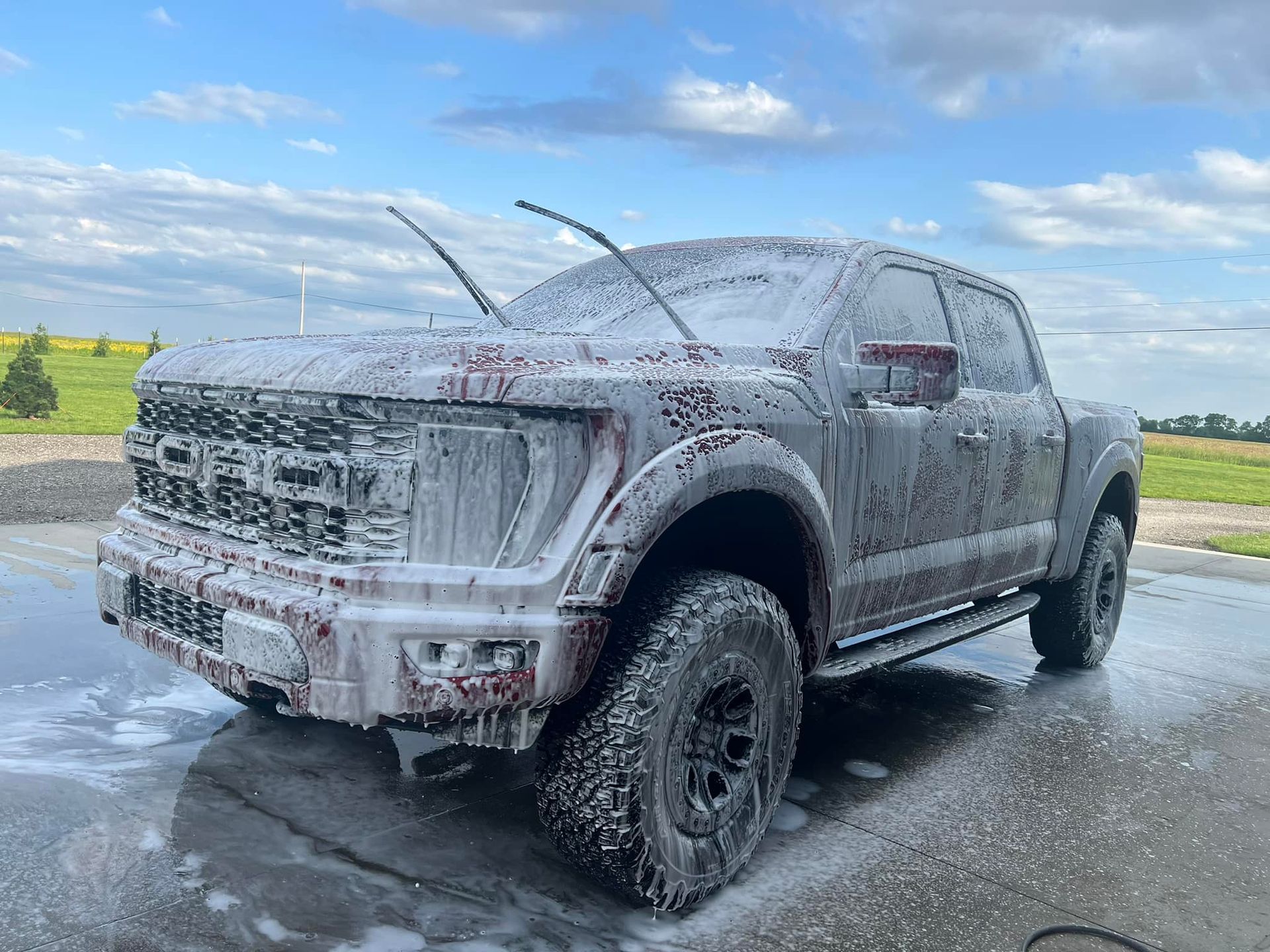 A dirty truck is covered in foam at a car wash.