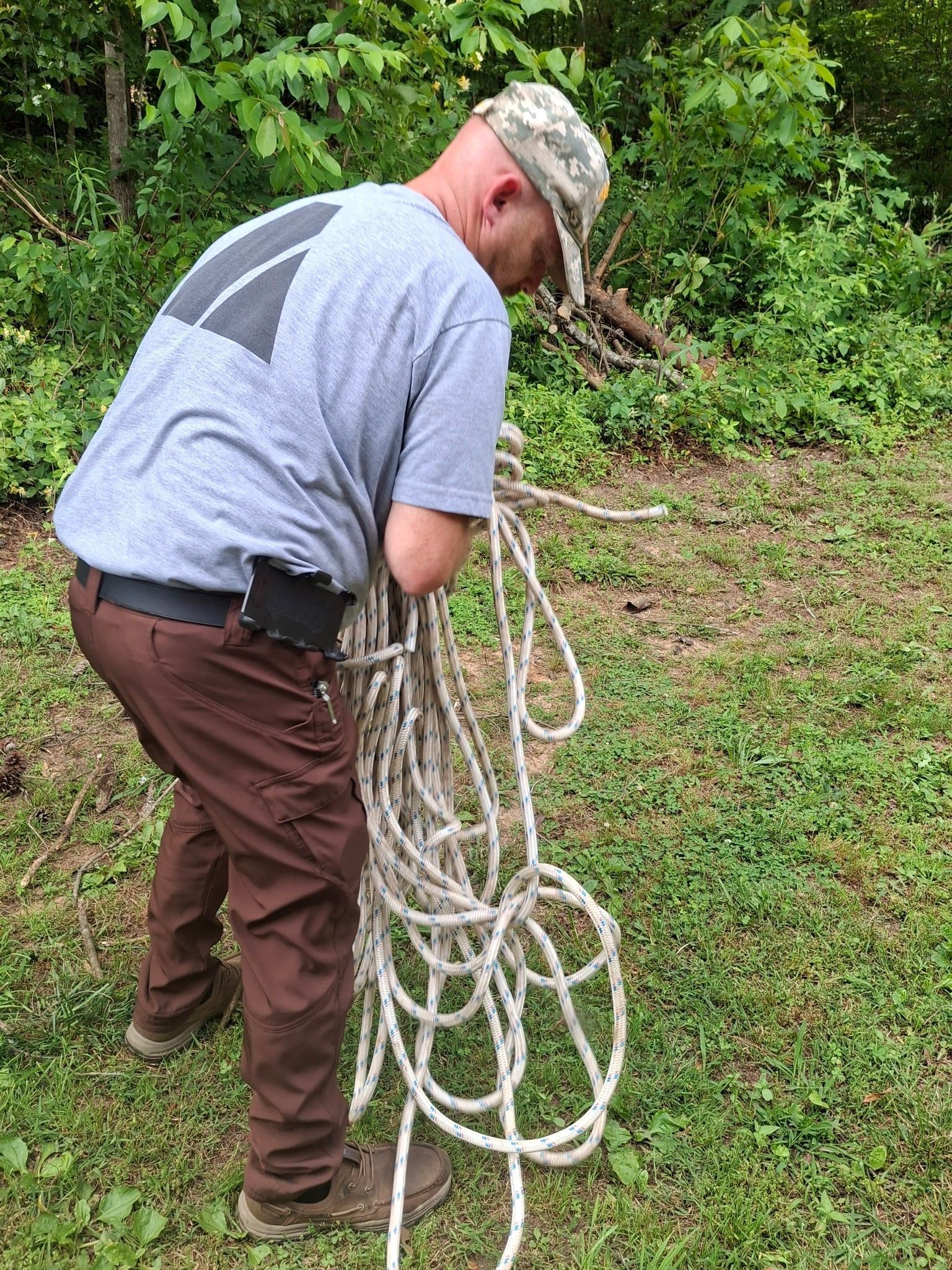 Man in brown pants and camo hat holding a thick, white rope outdoors.