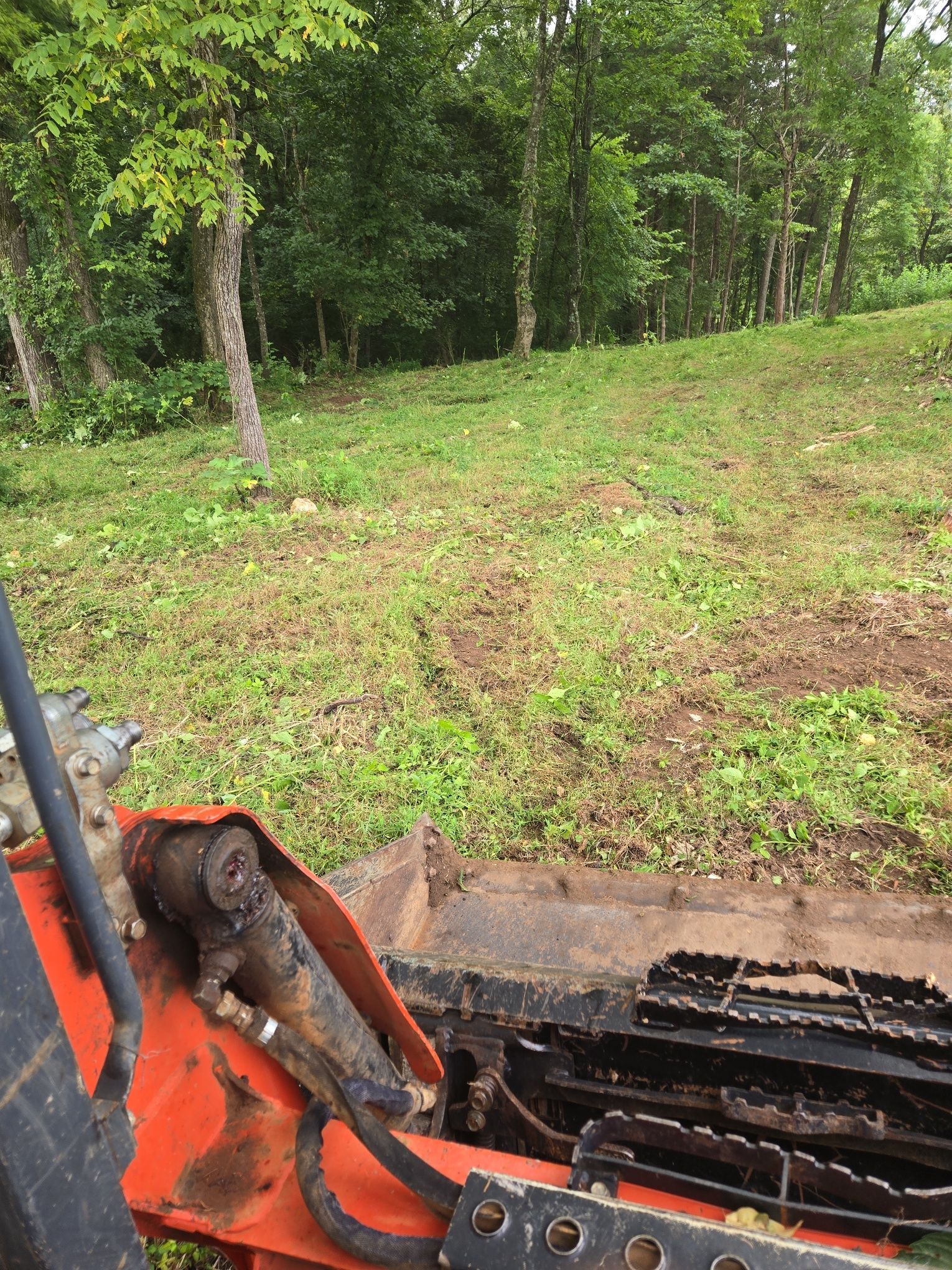 View from a tracked machine; grass, trees, and a hillside form the background.