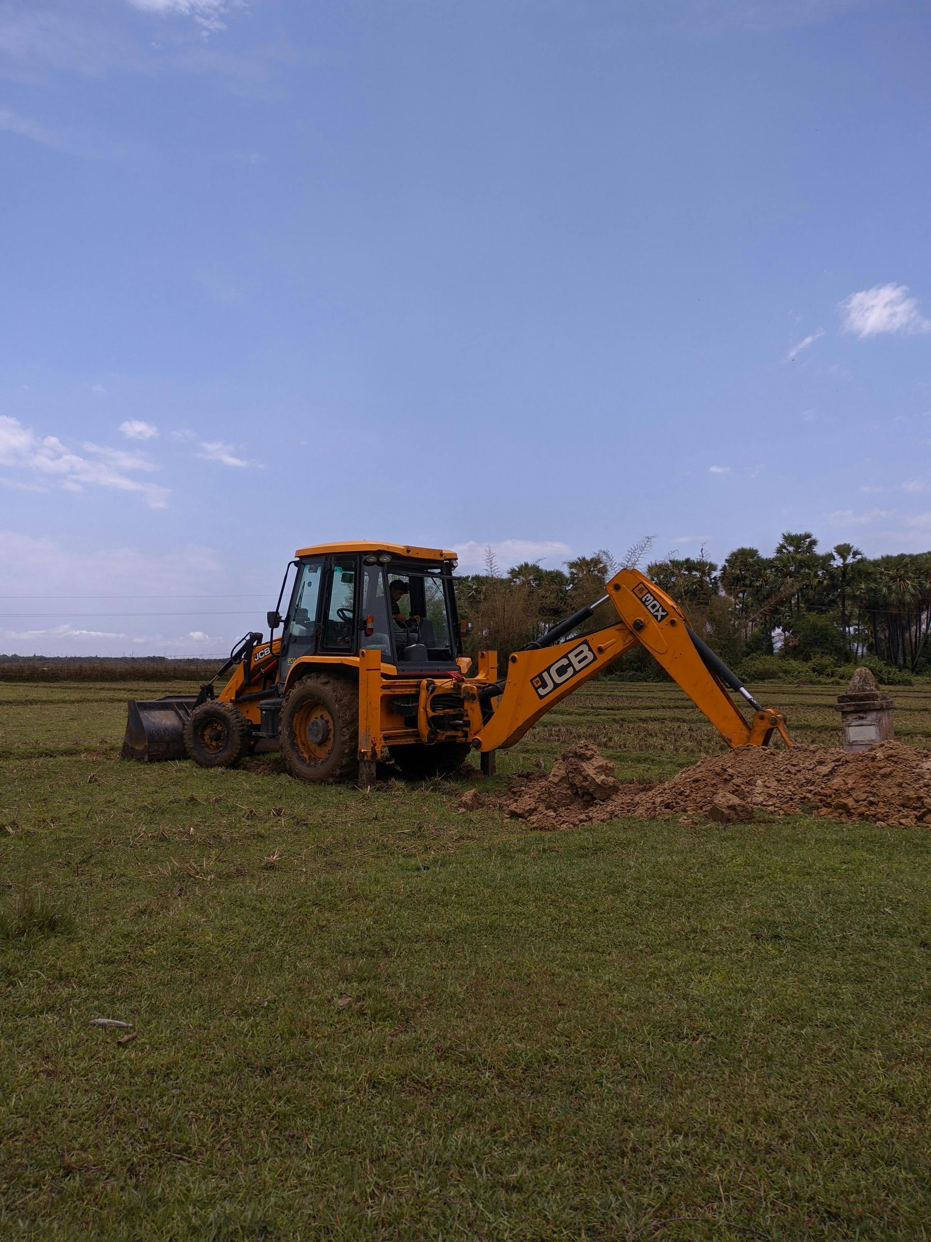 Yellow JCB backhoe excavator in a field, under a blue sky, digging.