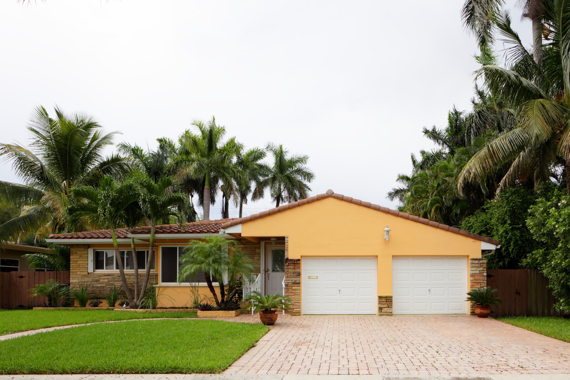 A house with two garage doors is surrounded by palm trees