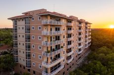 An aerial view of a large apartment building at sunset surrounded by trees.