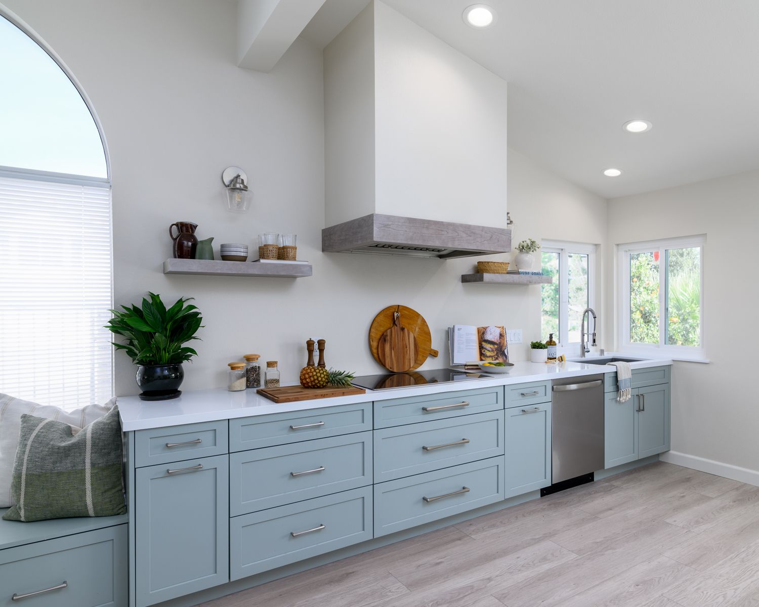 image of light green cabinets in a kitchen with white quartz countertops, custom hood over induction cooktop, light tan and gray luxury vinyl flooring, two floating shelves,  Rancho Conejo Neighborhood, Newbury Park, CA, open and airy kitchen remodel 