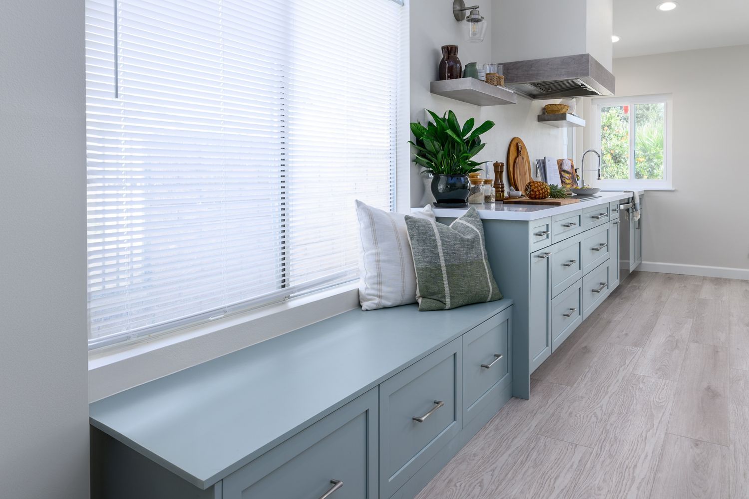 image of the side wall of a kitchen with a storage bench in the foreground, light green cabinets, custom hood, light tan and gray luxury vinyl flooring, floating shelves,  Rancho Conejo Neighborhood, Newbury Park, CA, open and airy kitchen remodel 