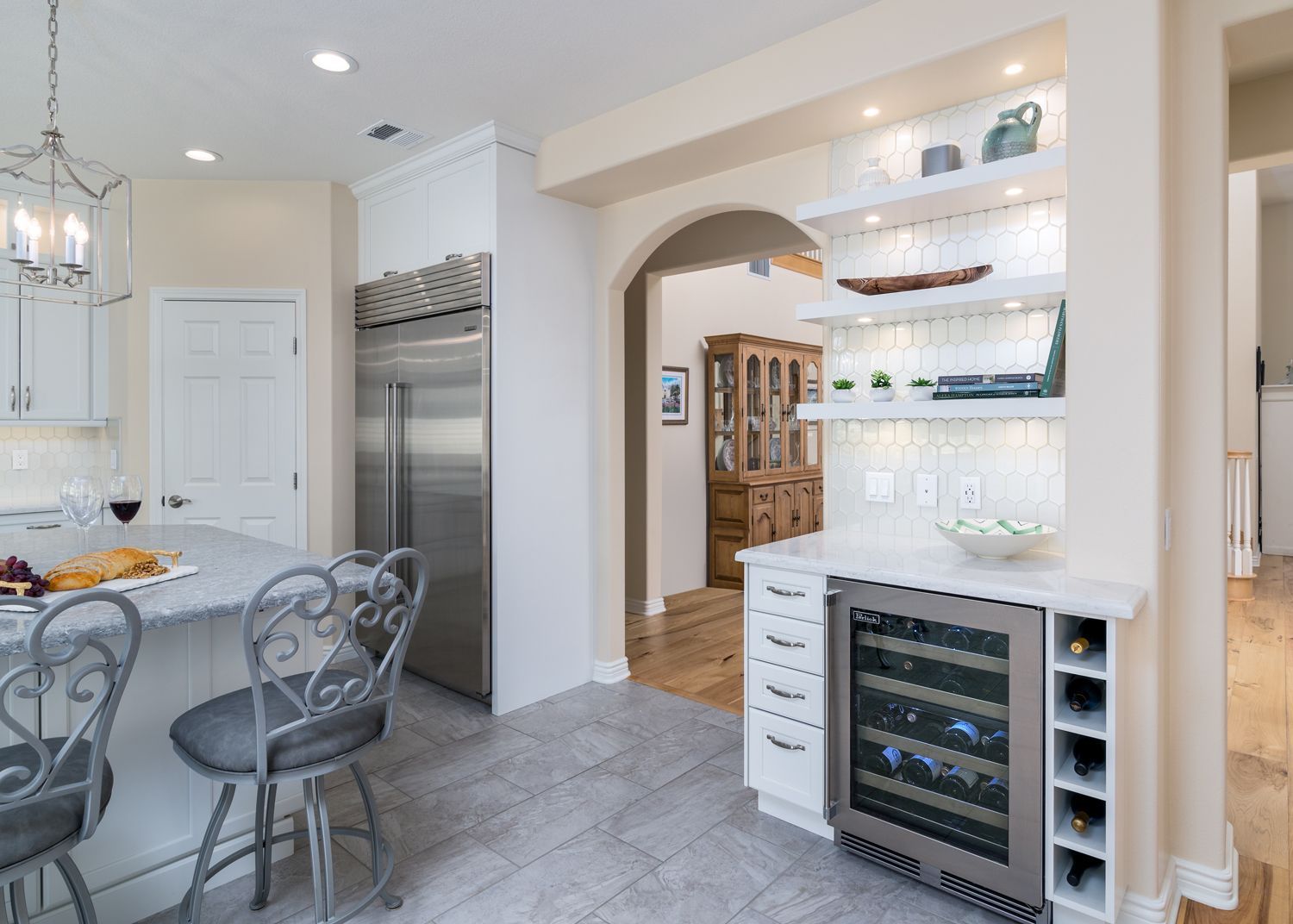 image shows a partial view of a kitchen leading to the dining room, new white painted DuraSupreme cabinetry encases mini fridge, wine cubbies, with floating shelves overhead, Kitchen remodel and expansion, Newbury Park, CA 