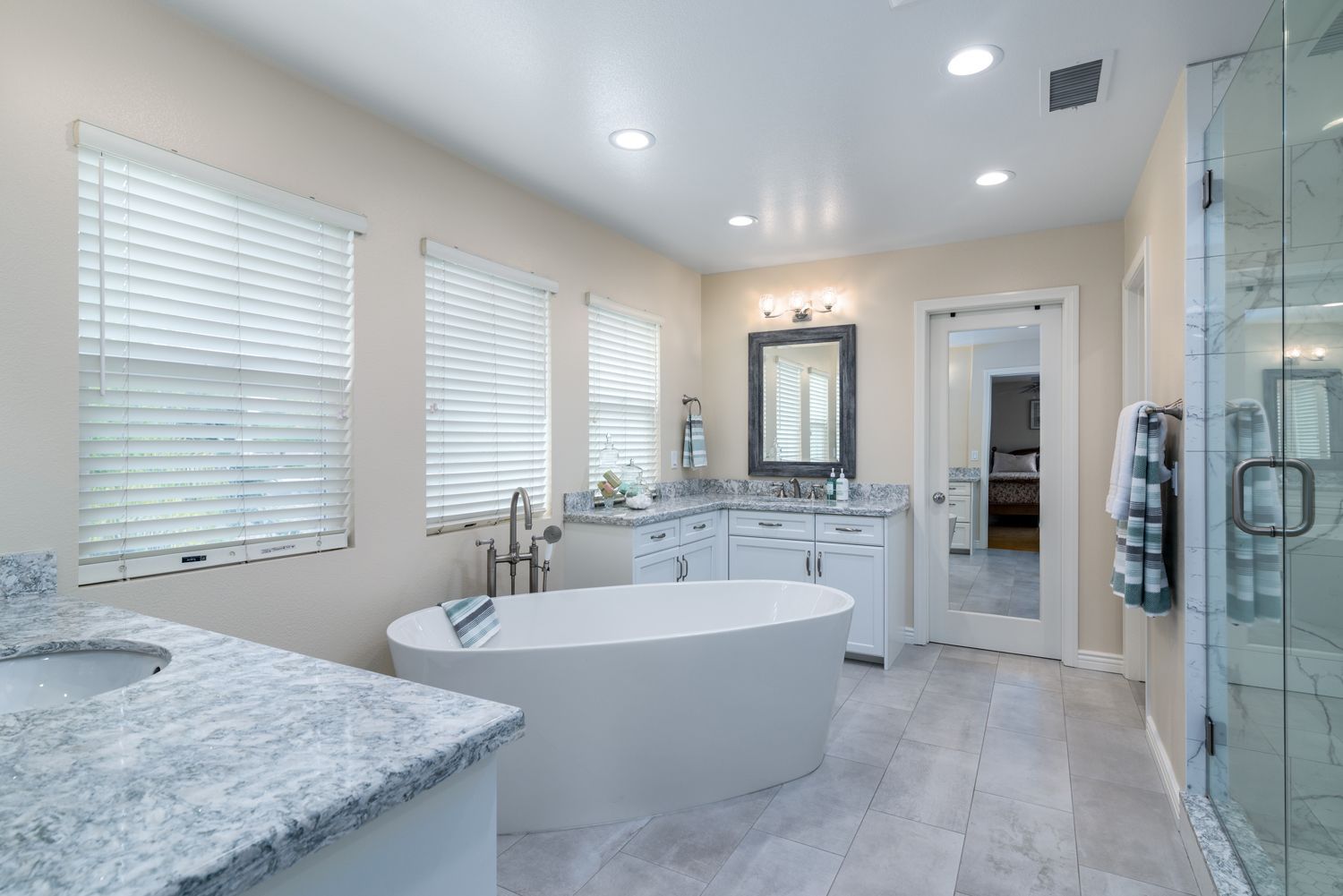 image shows a stylish primary bathroom with a free standing tub in the center and two white painted DuraSupreme on each side of the tub, Newbury Park, CA, Master Bathroom Remodel