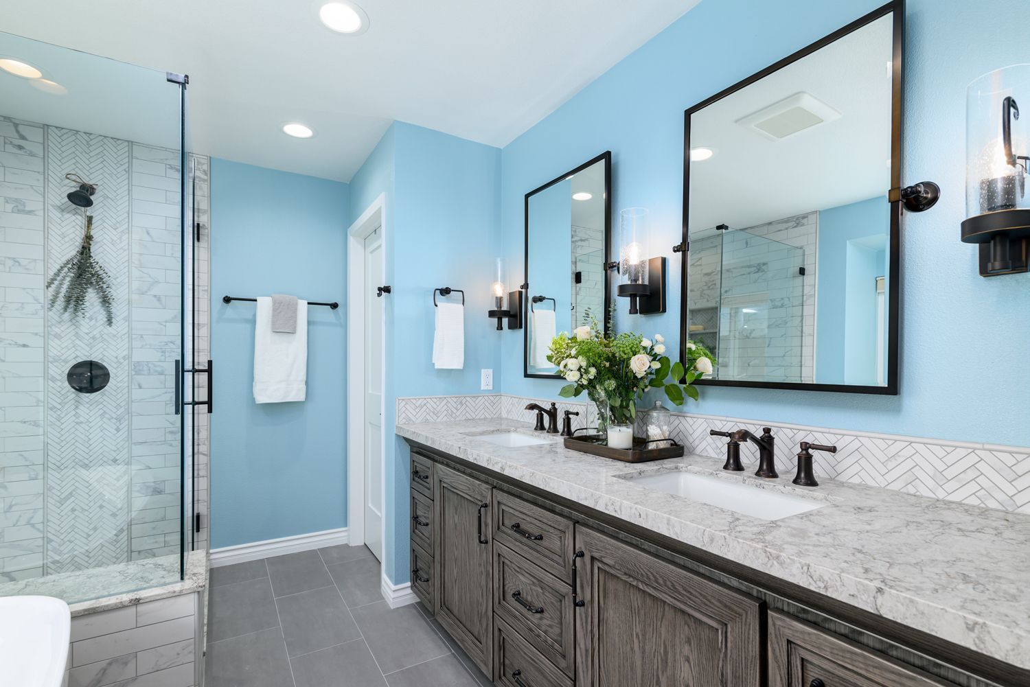 A bathroom with two sinks , two mirrors and a walk in shower.