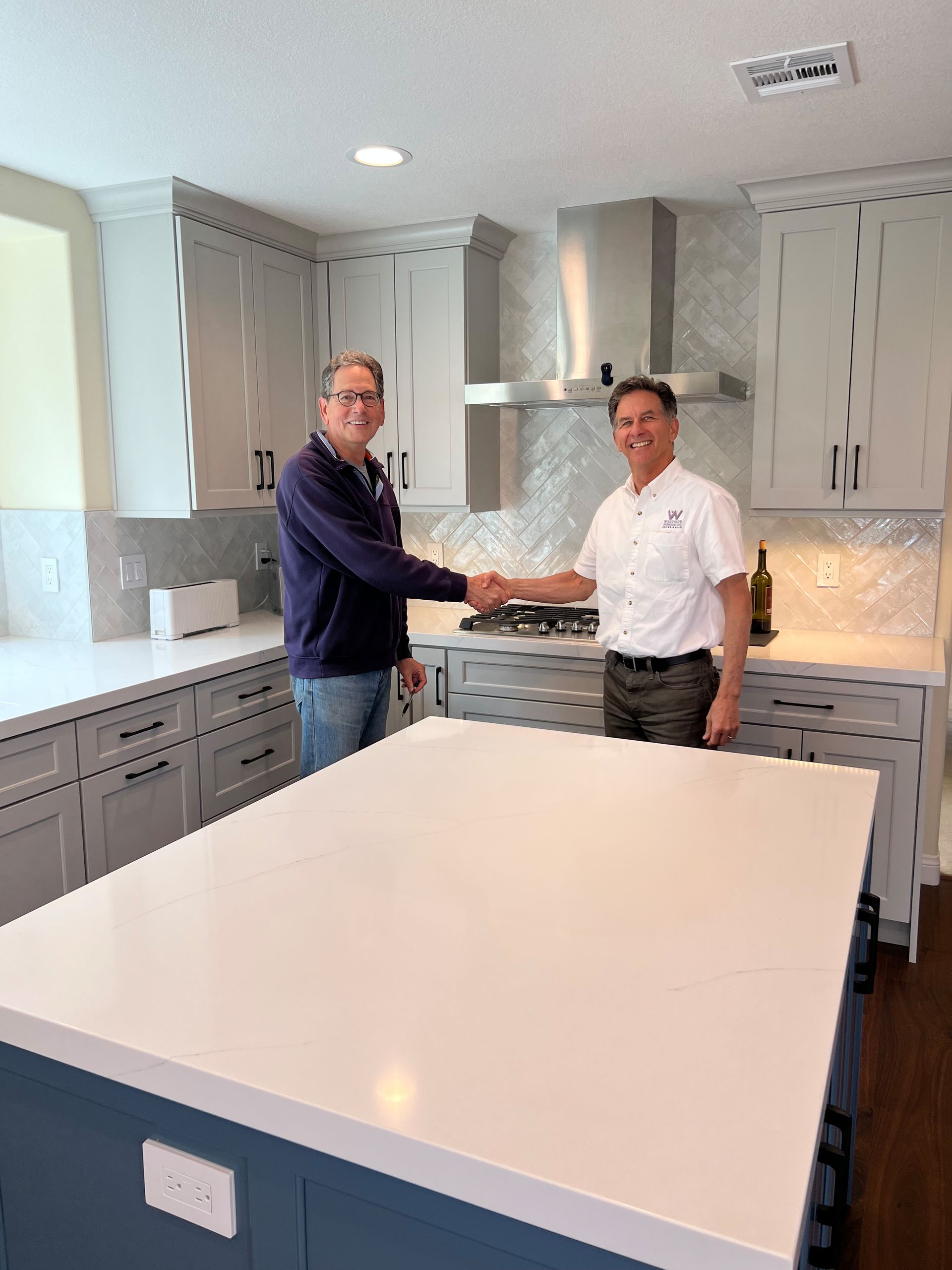image of a kitchen with an island with a white quartz countertop in the foreground and two men shaking hands in the background, image of happy homeowner and Bob Sturgeon, President of Westside Remodeling, Inc. Camarillo, CA kitchen remodel 