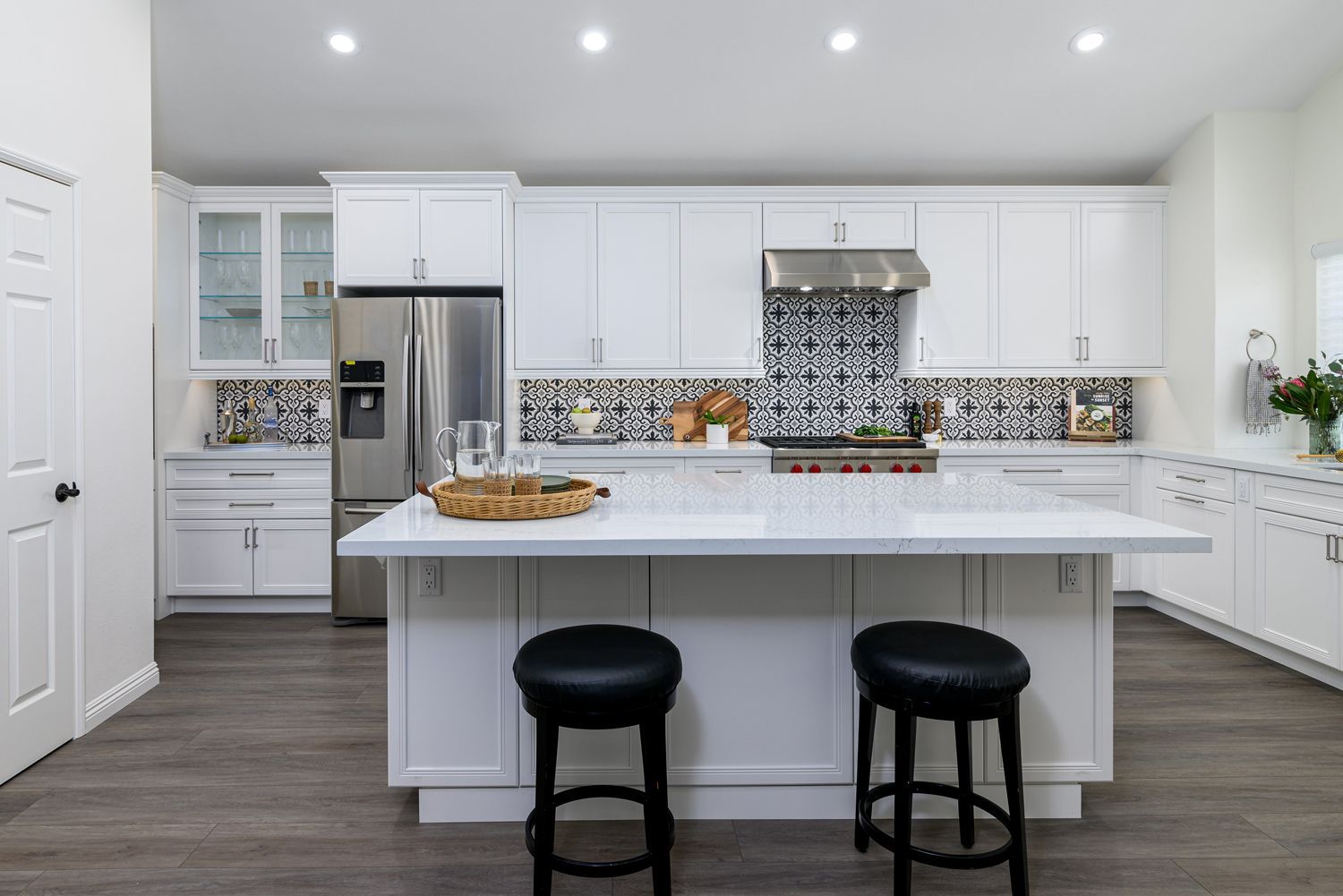 image of a white kitchen remodel, kitchen island with seating, thousand Oaks, CA, white cabinets, white quartz countertops, decorative patterned tile backsplash, stainless steel appliances, glass cabinet doors