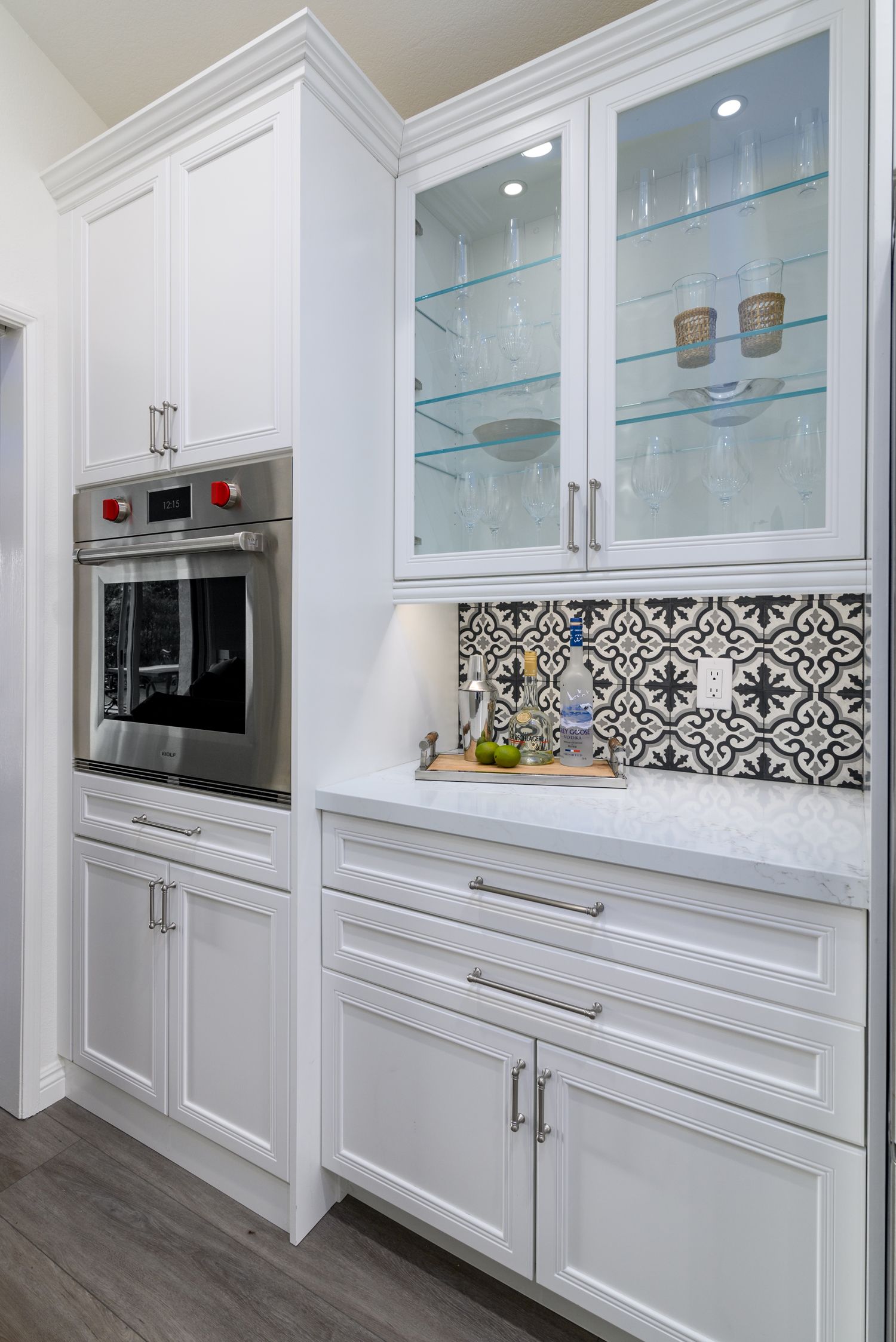 image of the bar area of a kitchen with cabinets, white quartz countertops, blue and red and white floral backsplash, stainless steel oven, glass shelves display wine glasses in cabinet Thousand Oaks, CA kitchen remodel, 
