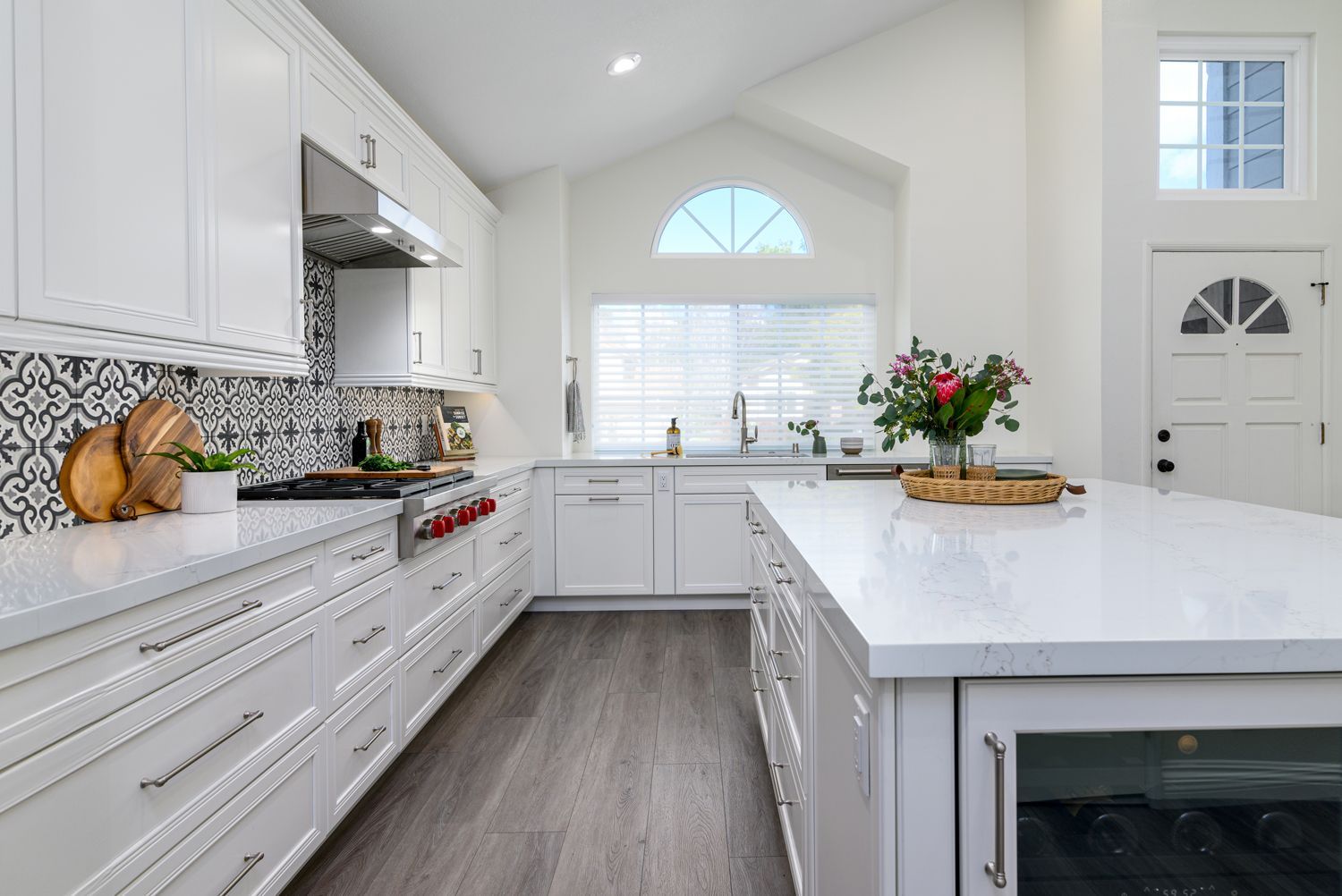 view of a kitchen from the back wall to the sink and window, kitchen island, white cabinetry, white quartz countertops, floral patterned fun backsplash, stainless steel hood, luxury vinyl gray flooring, Thousand Oaks, CA kitchen remodel, 
