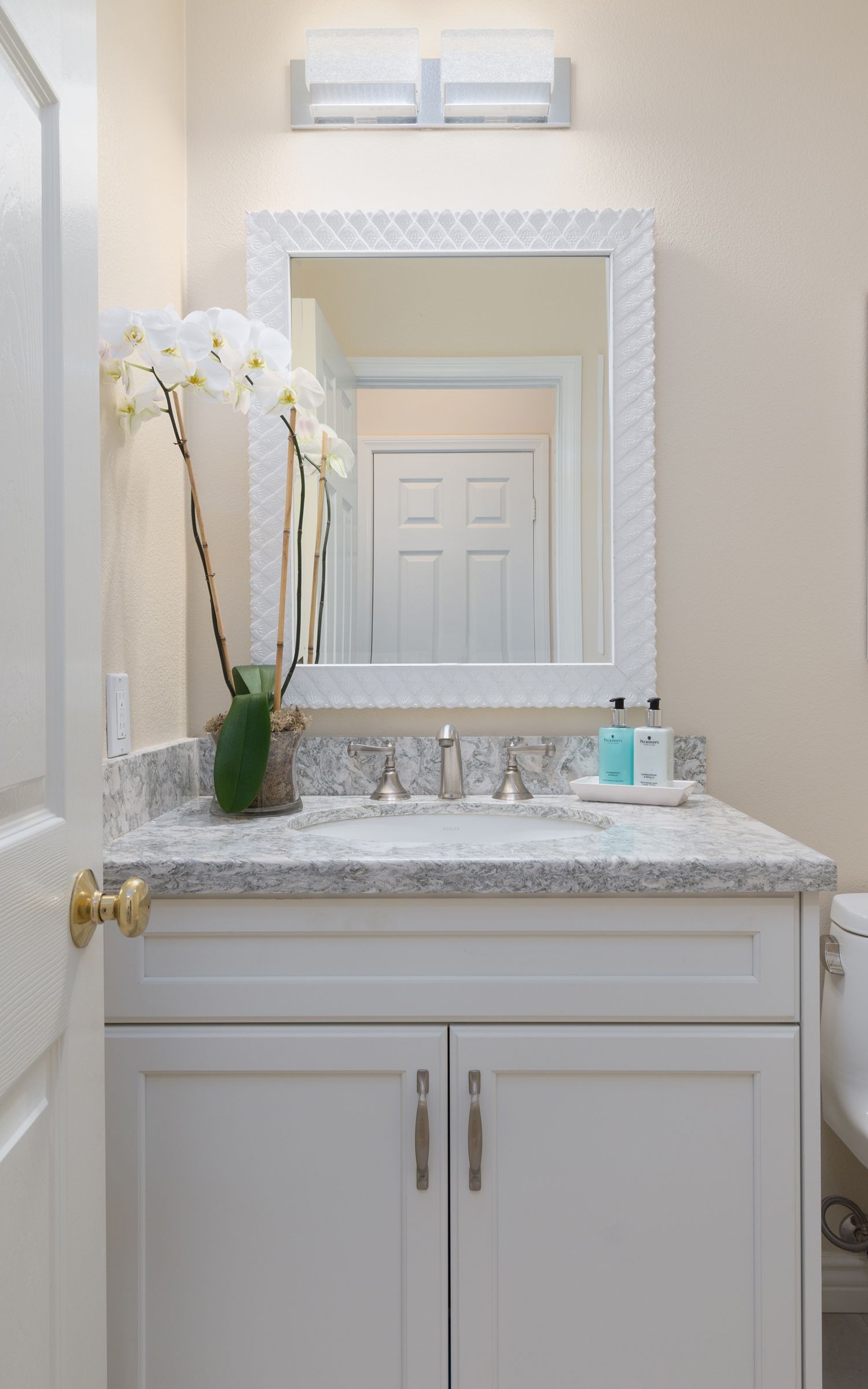 image shows the top of a small white powder bathroom vanity, swirling gray and white Cambria quartz countertops, sink, stainless steel faucet, white framed mirror overhead, Powder Bathroom Remodel, Newbury Park, CA 