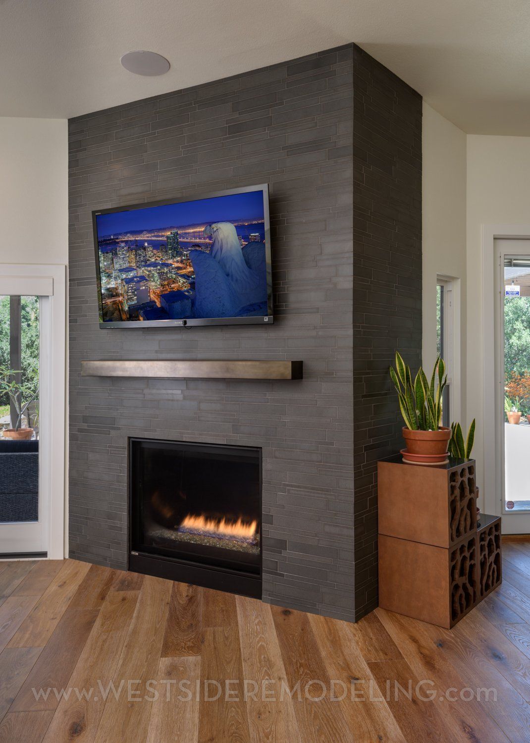 image shows a fireplace encased in dark stone with a metal mantel and flat screen tv above it, home remodel, Westlake Village, CA 