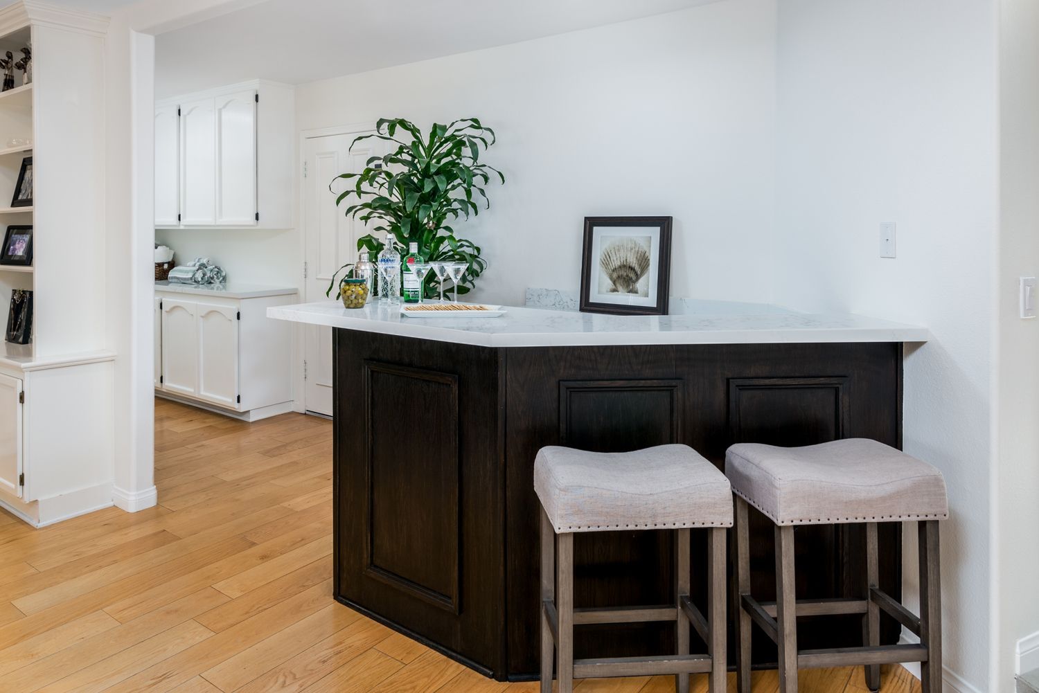 image of a small bar in dark brown wood with 2 seats in a family room with white linen cabinetry in the hall behind it, Omega Cabinetry, Oak Park, Ca Whole HOuse Remodel 