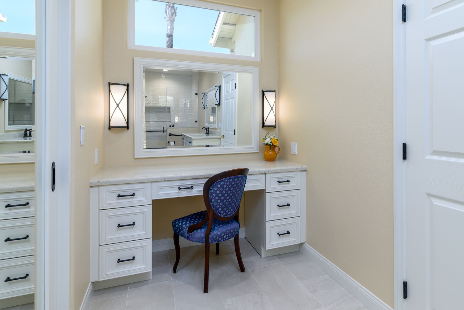 image of a make-up vanity with cream colored cabinets, blue chair, decorative rectangular mirror, wall scones, Primary Bathroom Addition, Thousand Oaks, CA 
