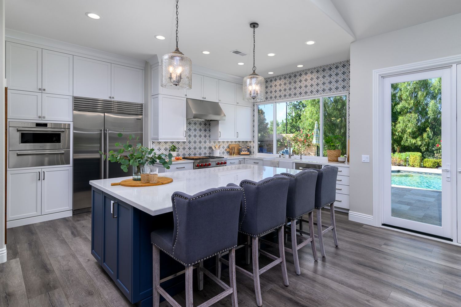 image shows a kitchen with a large dark gray-blue island in the foreground and white cabinets in the background, stainless steel appliances, luxury vinyl flooring, Newbury Park, CA kitchen remodel 