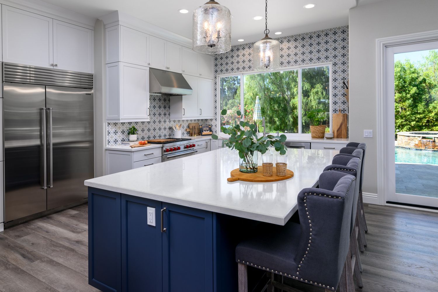 image shows a kitchen with a dark blue-gray island with white Quartz Countertops, gray bar stools, glass dome shaped light fixtures, Newbury Park, CA, kitchen renovation 