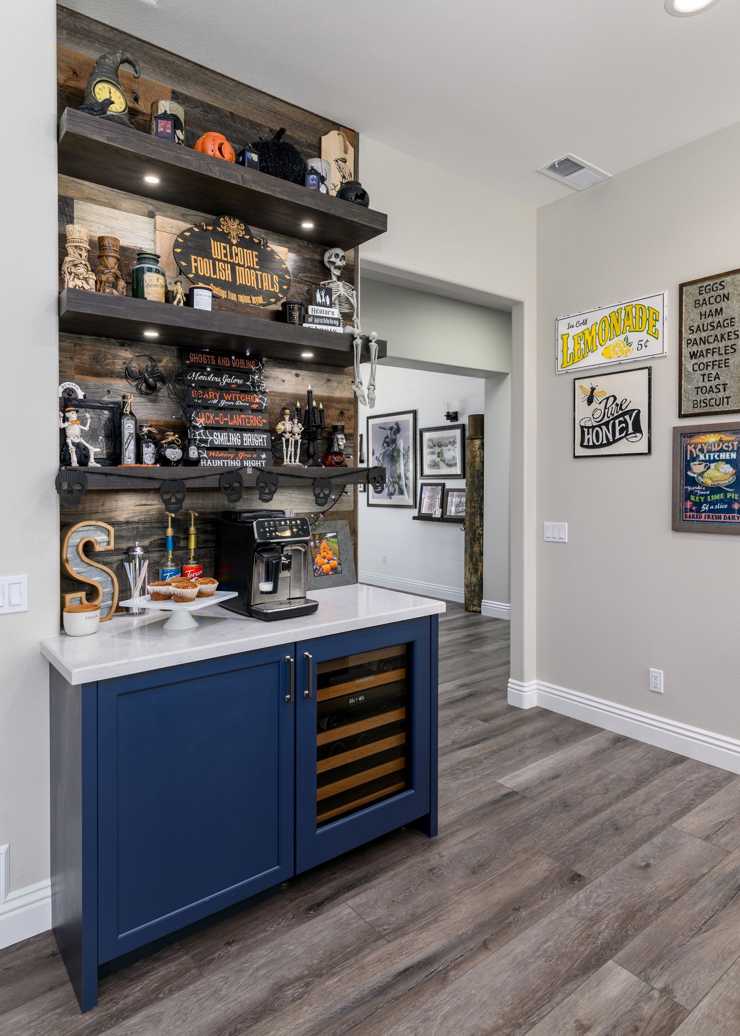 image shows a small blue cabinet with a white quartz countertop, a built in mini-beverage bar, a coffee station on the counter, wood accent wall with 3 floating shelves, Halloween decoration, Newbury Park, CA Kitchen Remodel 