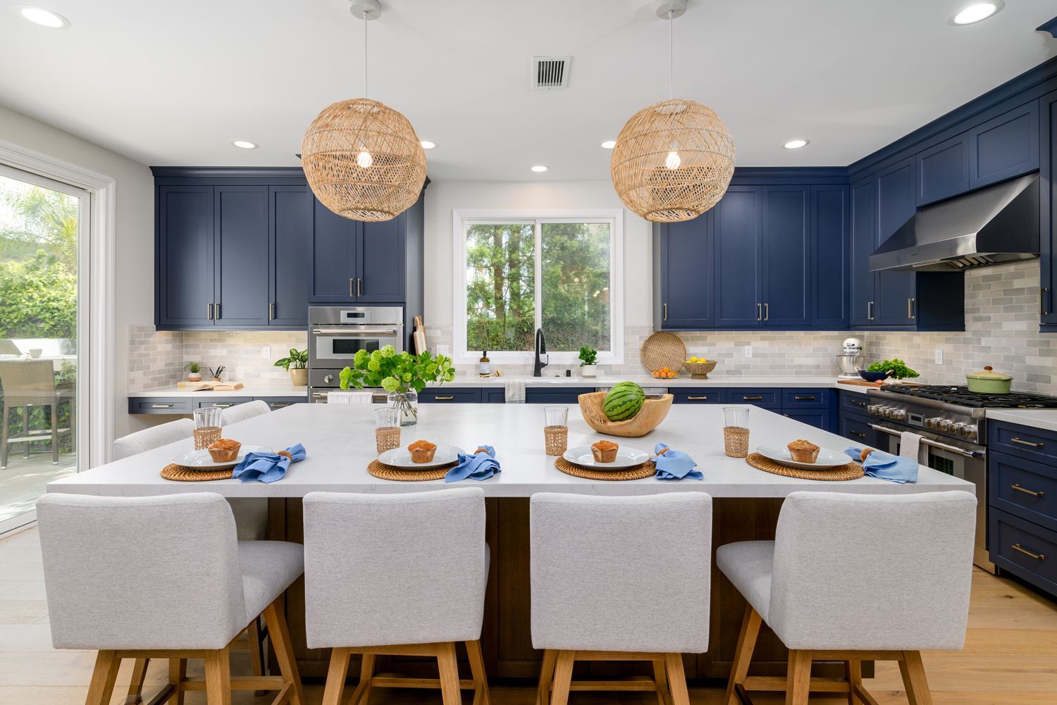 image of a large open floor plan kitchen with a large center island with bar height chairs, navy blue cabinets, Omega Full Access cabinetry, white quartz countertops, light gray and white subway tile backsplash, stainless steel Thermador appliances, new hardwood floors French Oak, woven pendant light fixtures over island, Milgard Window, Milgard sliding back door, Agoura Hills, CA modern style  Kitchen Remodel