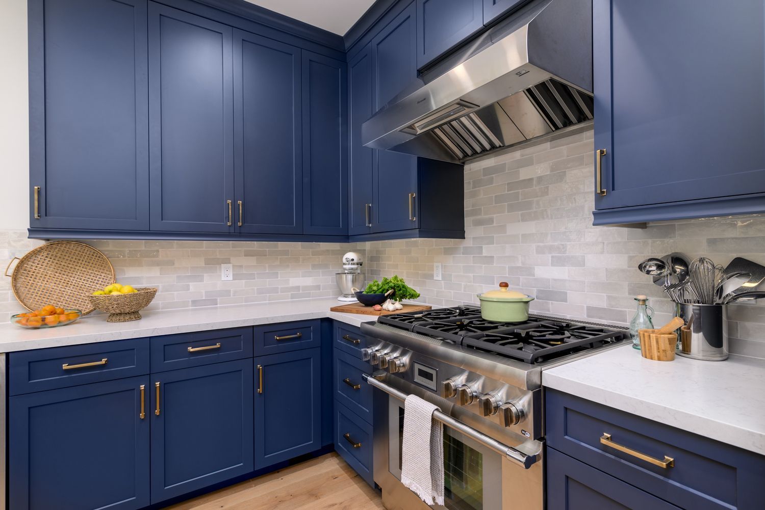 image the back corner of a kitchen with navy blue cabinets, Omega Full Access cabinetry, white quartz countertops, light gray and white subway tile backsplash, stainless steel oven, range and hood by Thermador appliances, new hardwood floors French Oak, Agoura Hills, CA, modern style Kitchen Remodel