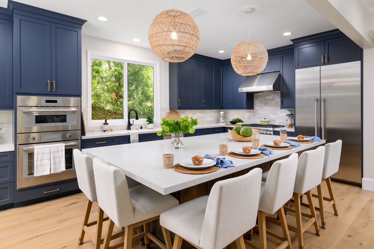 image of a large open floor plan kitchen with a large center island with bar height chairs, navy blue cabinets, Omega Full Access cabinetry, white quartz countertops, light gray and white subway tile backsplash, stainless steel Thermador appliances, new hardwood floors French Oak, woven pendant light fixtures over island, Milgard Window, Milgard sliding back door, Agoura Hills, CA, modern style Kitchen Remodel