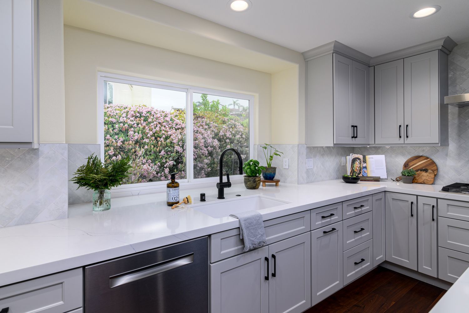 image of the back wall of a kitchen with a Milgard window, dishwasher, sink, light gray cabinets, white quartz countertops, herringbone patterned tile backsplash, Camarillo, CA Kitchen Remodel