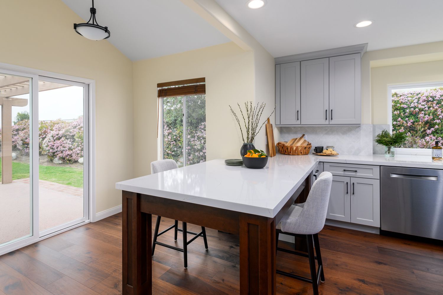 image of a dining area with a counter height table and two chairs, table has a white quartz countertop and a dark wood base , light gray kitchen cabinets on the back wall, luxurious dark stained wood floors, Camarillo, CA kitchen remodel