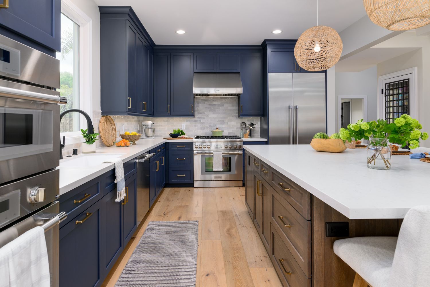 image down the back wall of a kitchen, navy blue cabinets by Omega Full Access, sink on the left and a kitchen island with medium brown stain on the right, white quartz countertops, light gray and white subway tile backsplash, stainless steel Thermador appliances, new hardwood floors French Oak, woven pendant light fixtures over island, Agoura Hills, CA, modern style Kitchen Remodel