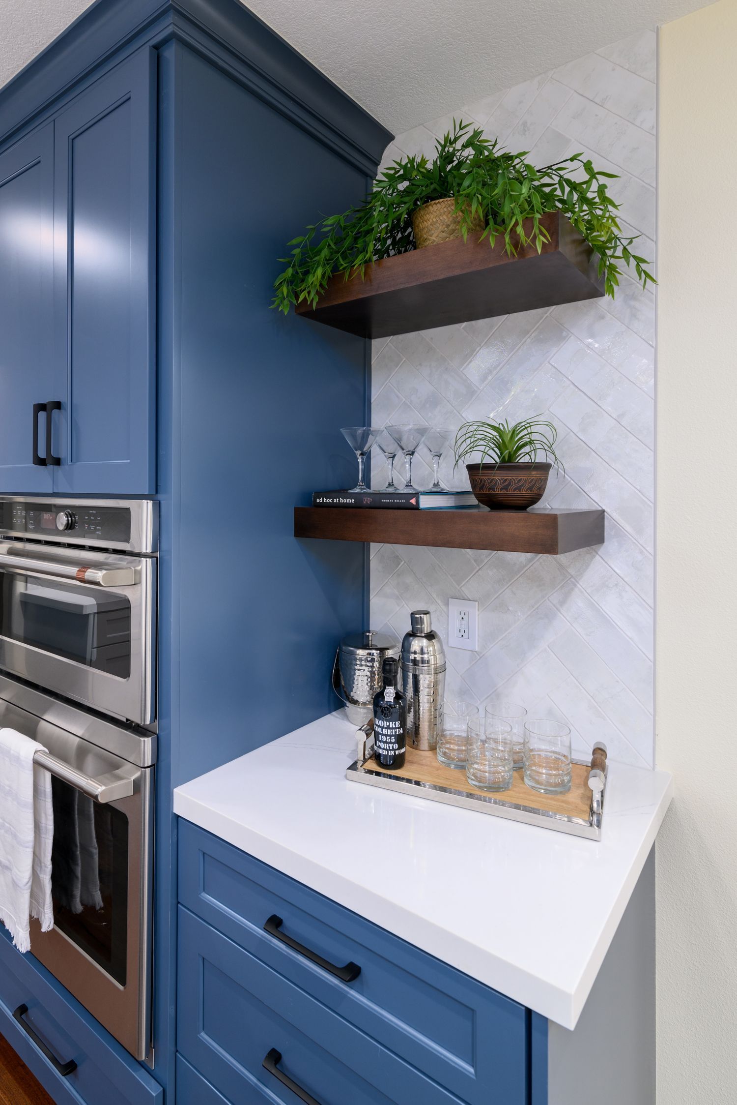 image of a section of a kitchen with royal blue cabinets, white quartz countertop, floating shelves made of dark wood, steam oven, oven, herringbone backsplash, Camarillo, CA kitchen remodel 