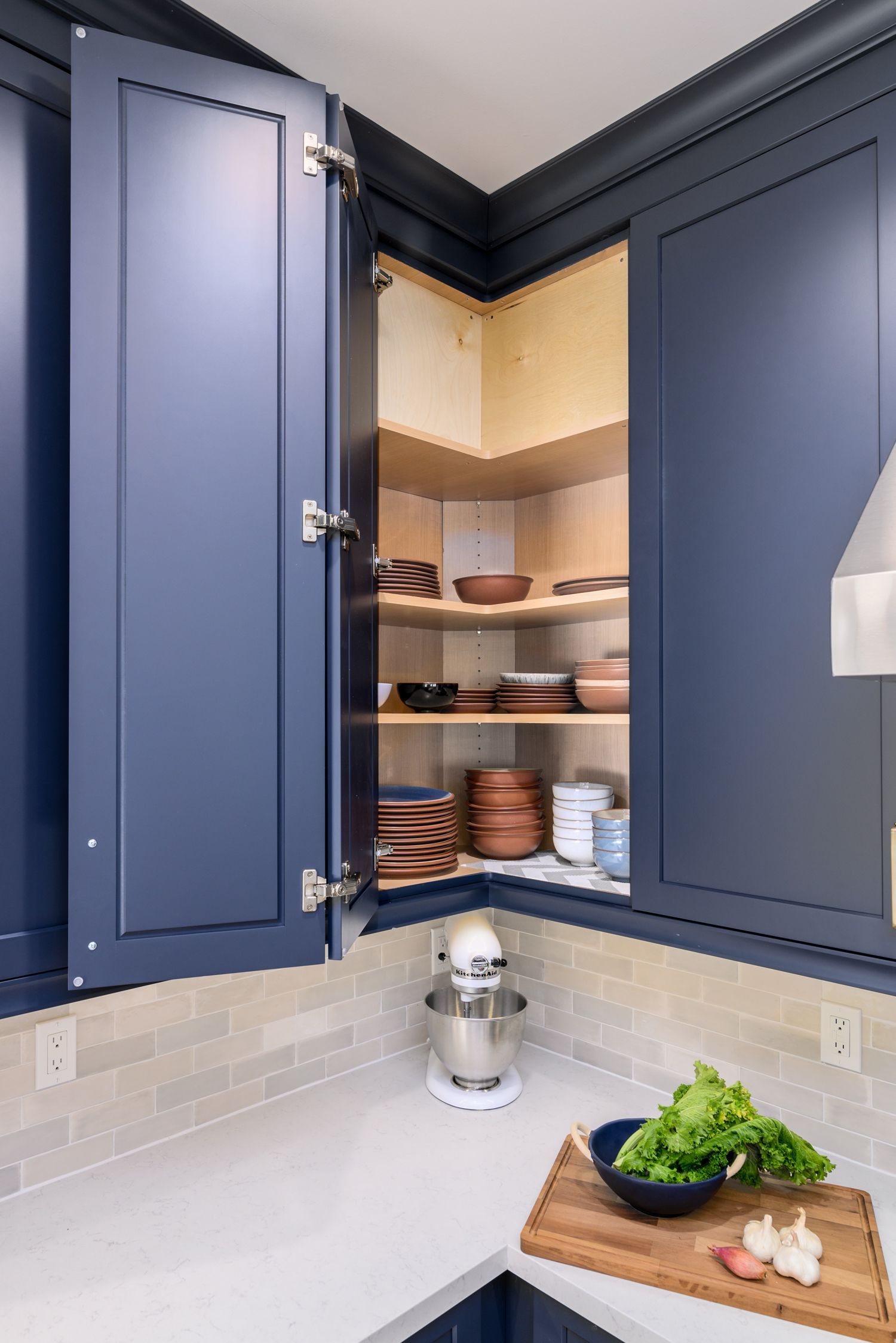 image of the back corner of a kitchen with corner cabinet opened to display lazy susan custom storage feature, navy blue cabinets, Omega Full Access cabinetry, white quartz countertops, light gray and white subway tile backsplash, Agoura Hills, CA, modern style Kitchen Remodel