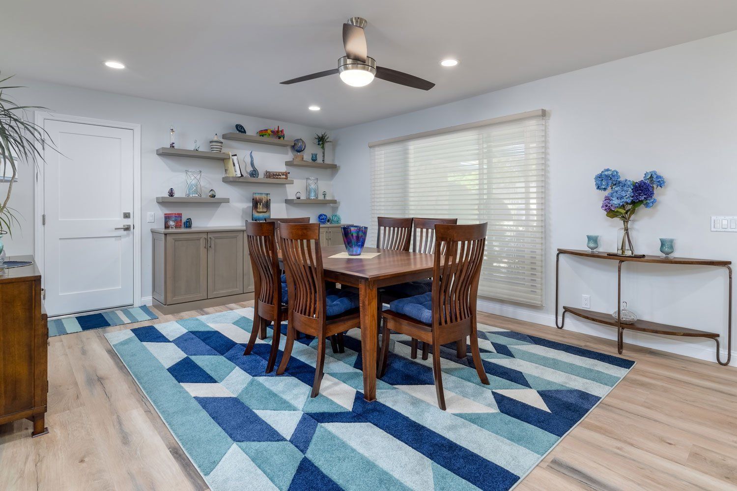 image shows a dining room with a mission style dining set, light wood cabinetry and floating shelves in the background, blue patterned rug, West Hills, CA home remodel 