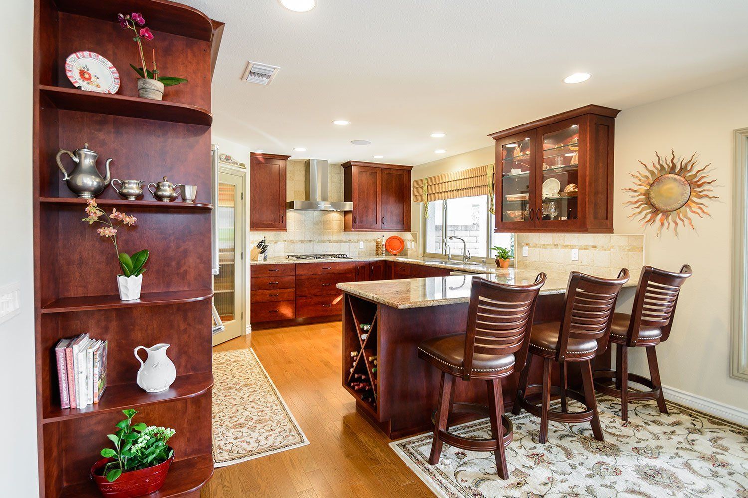 A kitchen with a large island , stools , shelves and a rug.