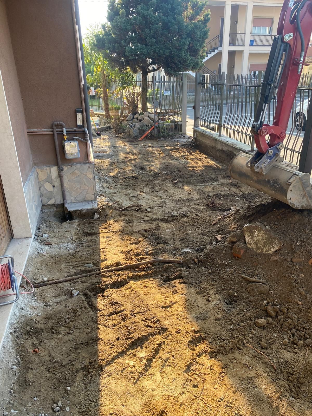 Un escavatore rosso sta scavando una buca nel terreno davanti a una casa.