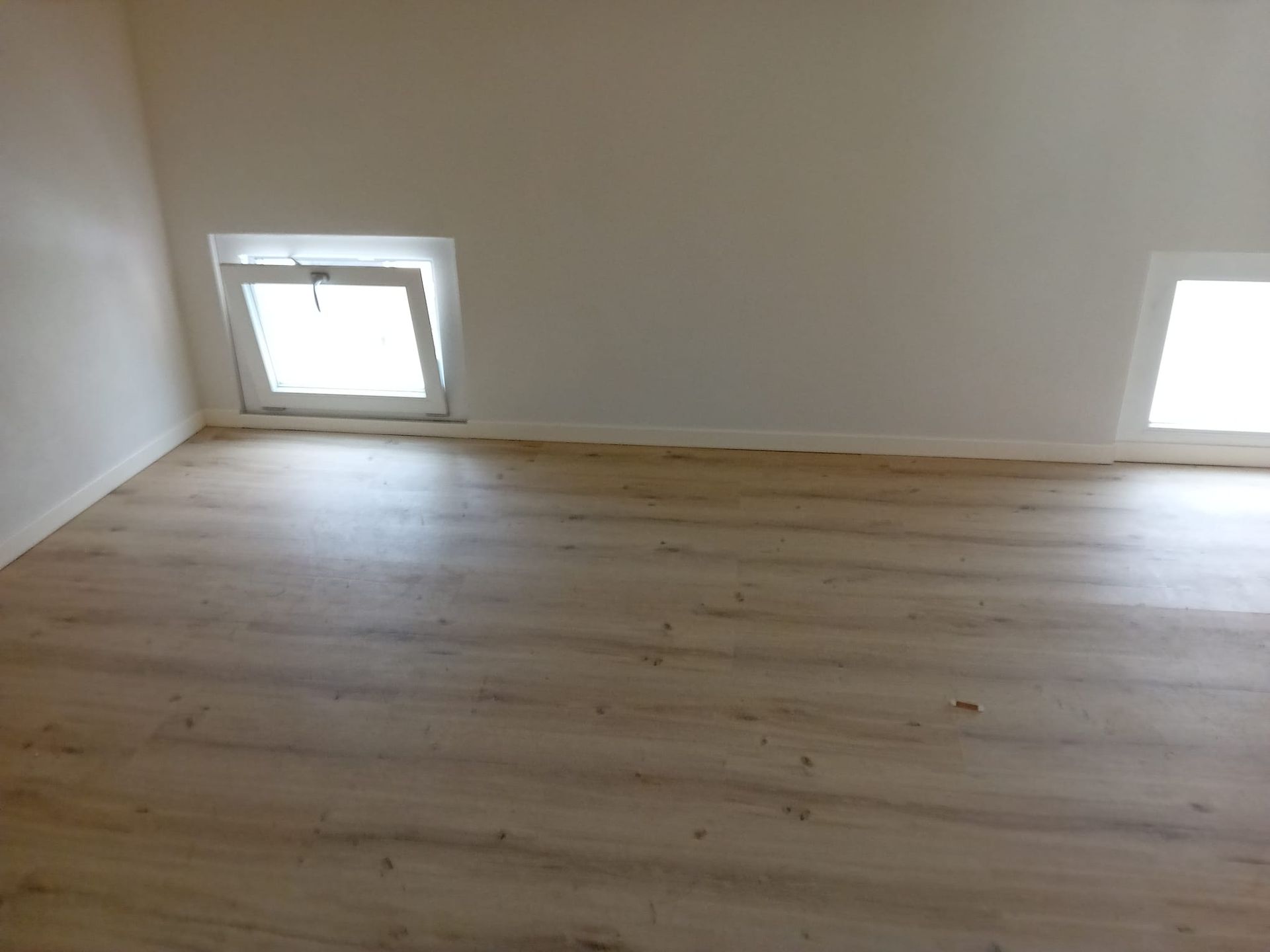 Una stanza vuota con pavimento in legno e due finestre.