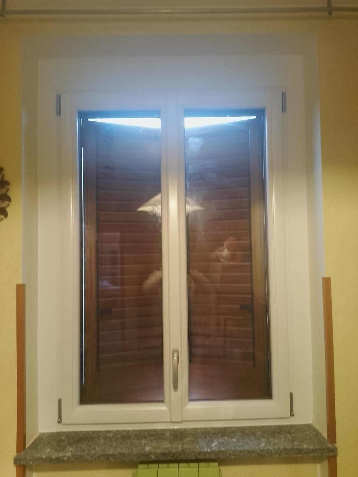 Una finestra bianca con persiane è appoggiata sul davanzale di una stanza.