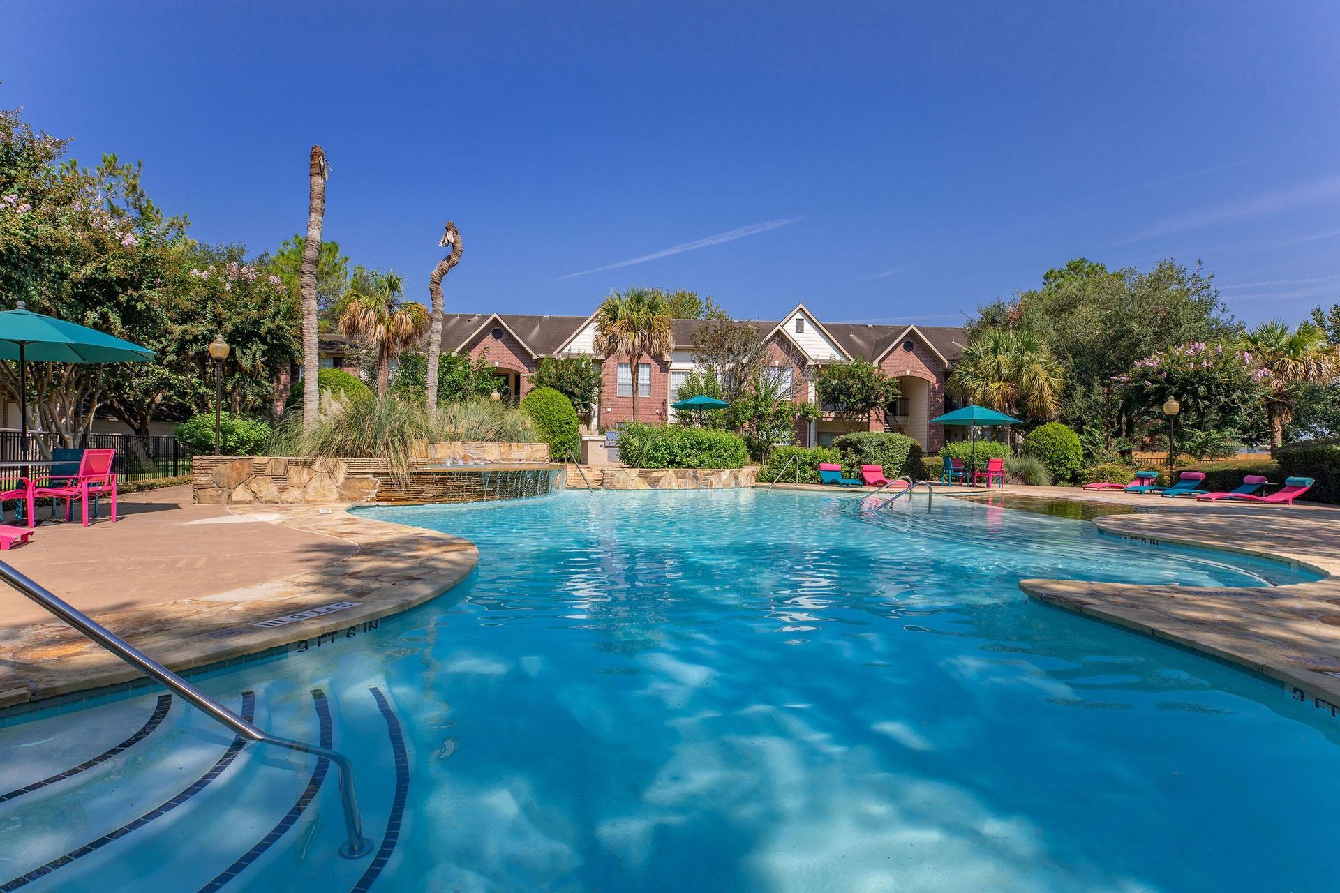 A large swimming pool surrounded by chairs and umbrellas in front of a house at Windsor Estates.