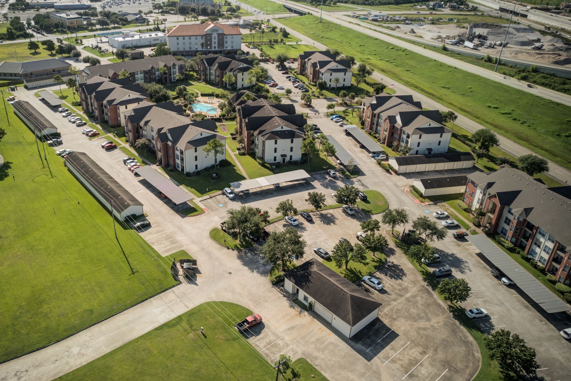 Outdoor patio with grill, lounge chairs, table, and umbrella near a building with trees.