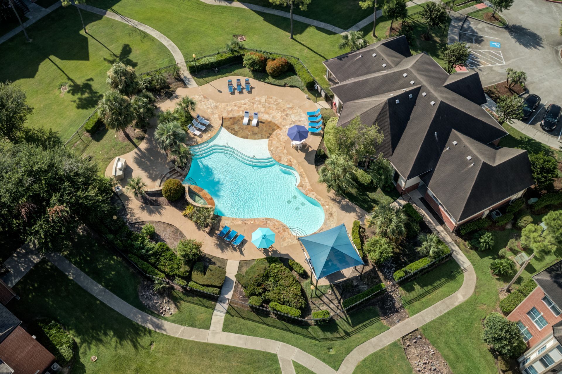 Pool with lounge chairs, umbrellas, and buildings in the background under a blue sky.