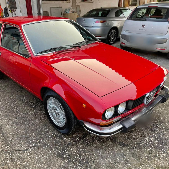 Vista frontale di una coupé Alfa Romeo rossa d'epoca parcheggiata. Dettagli cromati, cerchi argentati.