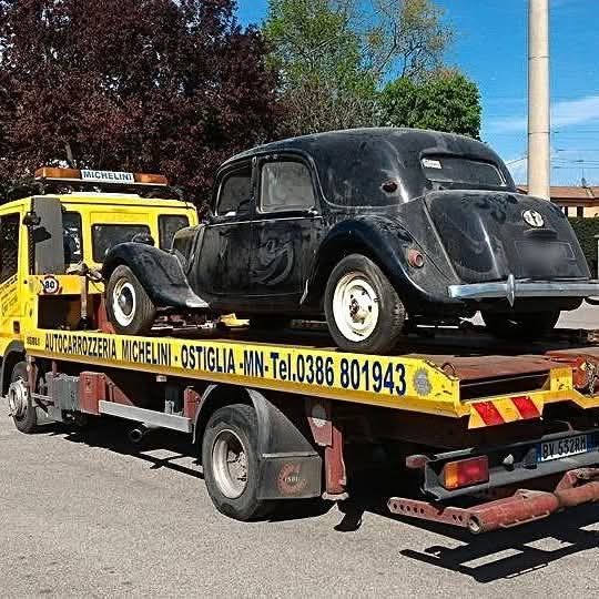 Un'auto d'epoca nera viene trainata da un carro attrezzi giallo. Il camion è parcheggiato all'esterno.