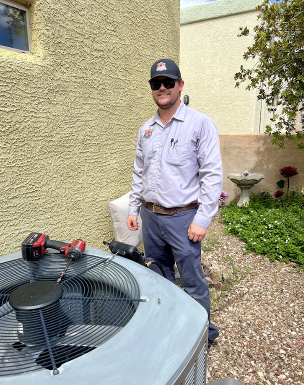 A man wearing sunglasses and a hat is standing next to an air conditioner.