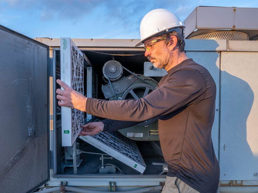 A man wearing a hard hat is changing a filter on an air conditioner.