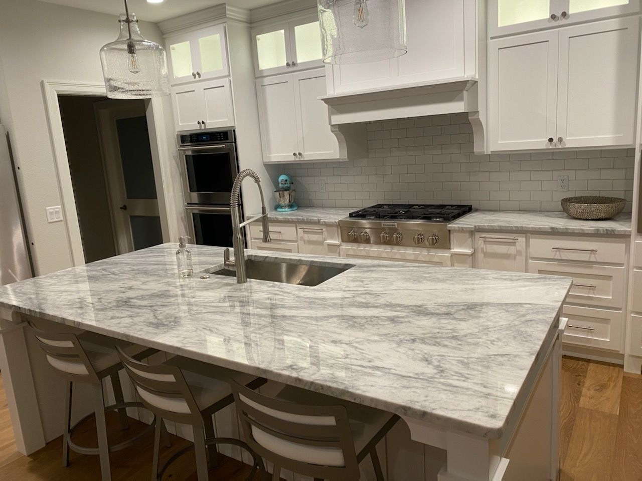 A kitchen with white cabinets , granite counter tops , stainless steel appliances and a large island.