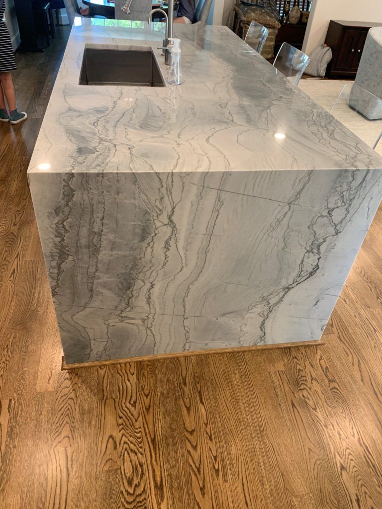 A kitchen island with a sink and a marble counter top.