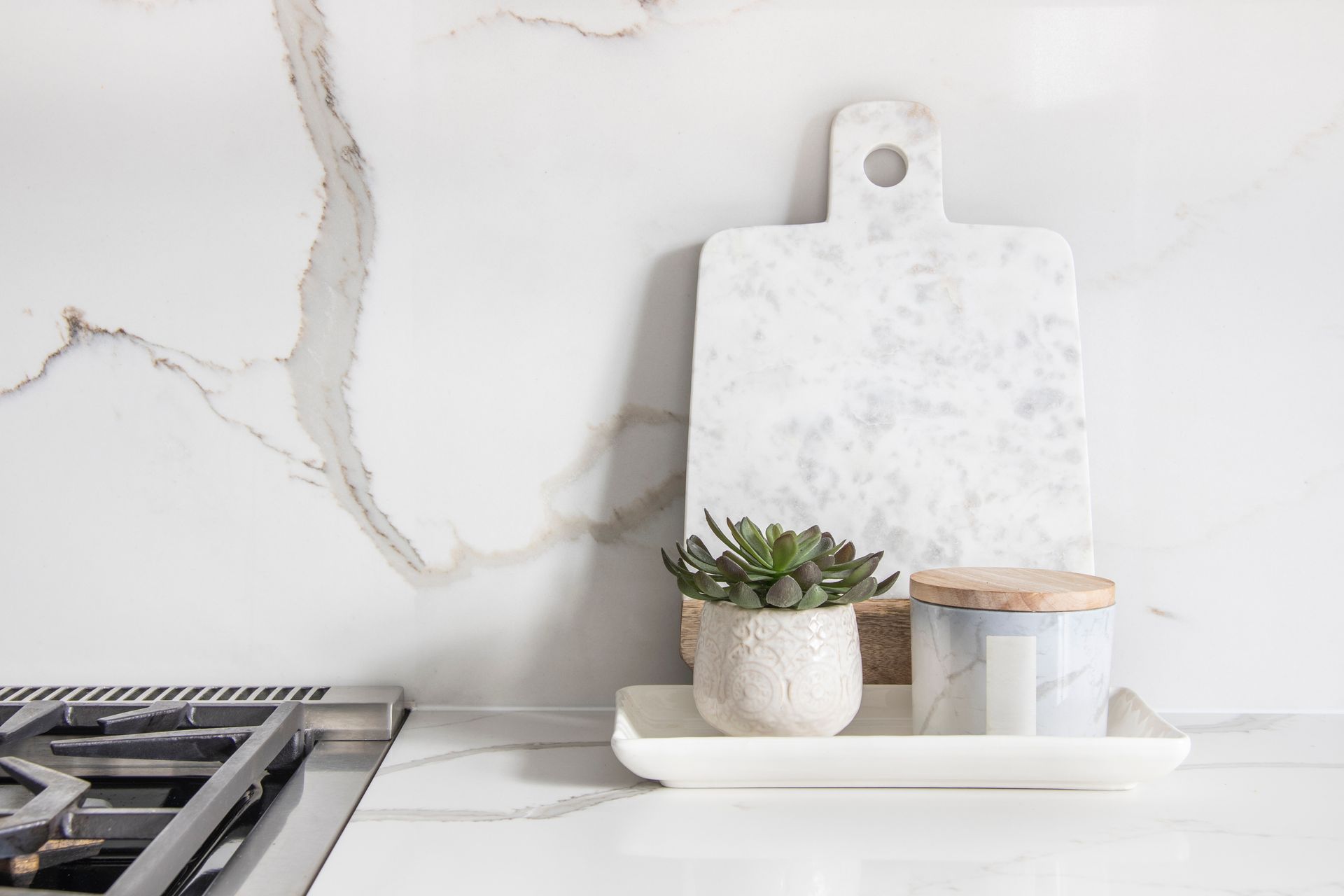 A cutting board and a potted plant are on a tray on a kitchen counter.